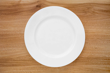 Round white plate on a wooden table. View from above
