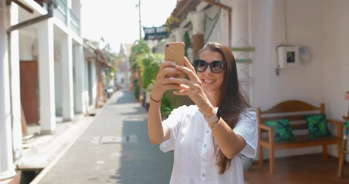 Attractive woman with a smartphone walking through the streets of Galle Fort. A girl taking pictures of herself and buildings of the former colony. tracking shot. in slow motion 