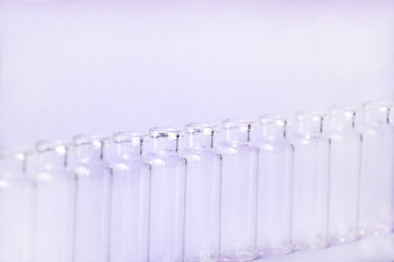Empty glass medical vials, ampoules in a row on a light violet background with space for text. Glass medical bottles with selective focus. Vaccines, Medicine, Laboratory, Immunization concept.