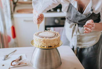 A middle aged woman pastry chef or baker prepares a cake and decorates it with icing.
