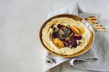 Traditional classic Mediterranean hummus of chickpeas with olive oil served with cherry tomatoes,roasted beets and micro greens with copy space for text.Healthy and nutritious dietary vegan snack