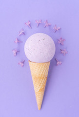 Composition of ice cream cone with bath ball on a violet background. Bathroom cosmetic accessories. Flat Lay. Top View. Lilac flowers