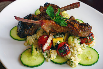 Dish of sliced lamb rack on zucchini slices and Israeli couscous