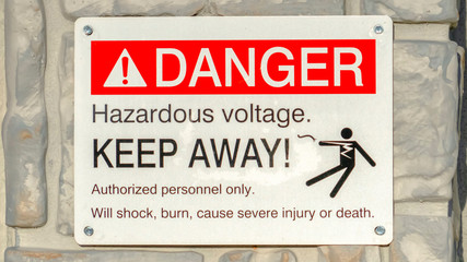 Clear Panorama Close up of Danger Hazardous Voltage Keep Away sign posted on a gray surface