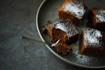 Delicious healthy vegan moist dairy-free dark chocolate brownies dessert or square sponge cakes cooked without eggs and decorated with powdered sugar on a dark textured background with copy space