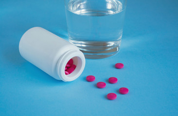 Bottle with pink pills and a glass of water on a blue background. Concept medicine, health, pharmacology