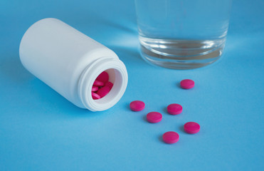 Bottle with pink pills and a glass of water on a blue background. Concept medicine, health, pharmacology