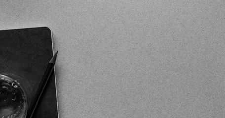 empty gray office desk top view with black notebook, pencil and a glass of water with space for text, banner concept, mockup for business