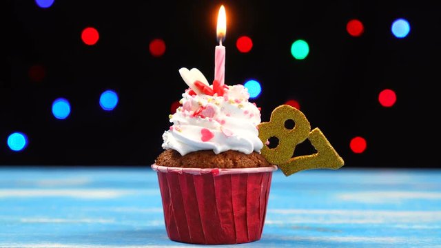 Delicious birthday cupcake with burning candle and number 87 on multicolored blurred lights background