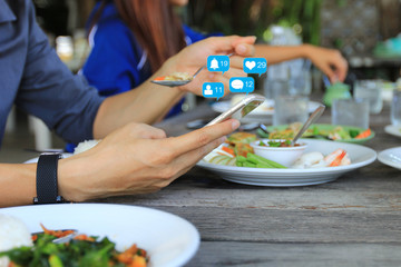 Hand holding smartphone for checking social media with icon or hologram in restaurant, Communication network internet and Business concept