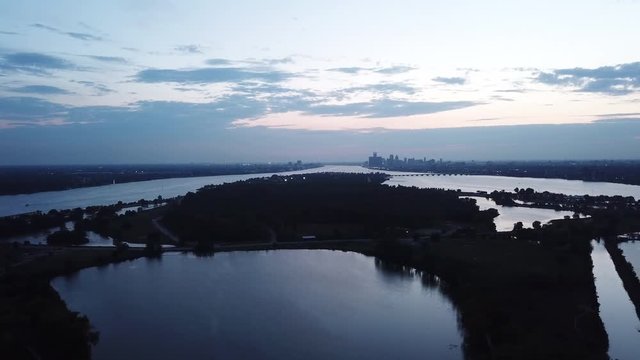 Belle Isle Detroit aerial view at sunset on a summer day. Bridge, buildings, boats visible in the distance. Island silhouette on the Detroit river with the Detroit skyline in the background.