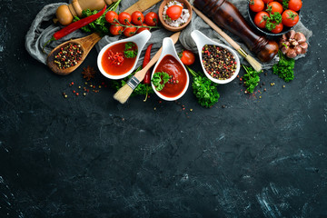 A set of tomato sauces on a black stone background. Ketchup, barbecue sauce, tomato sauce. Top view. Free space for your text.