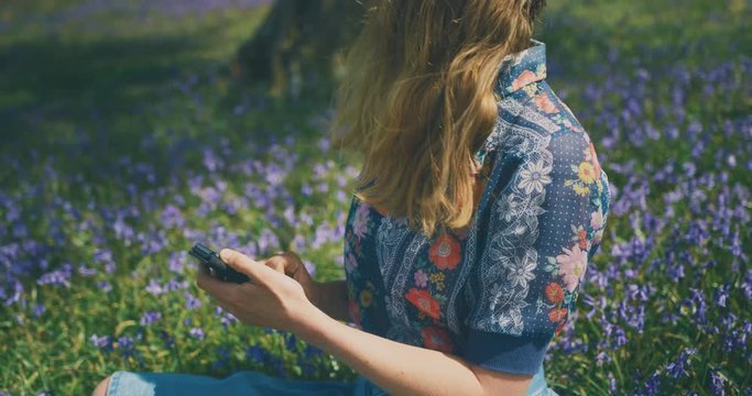 Young woman using smartphone in field of bluebells