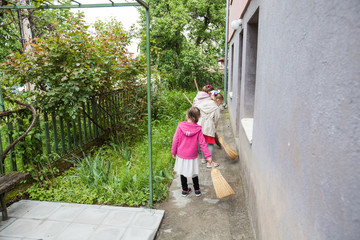 Fototapeta na wymiar Three little girls cleaning backyard with broom