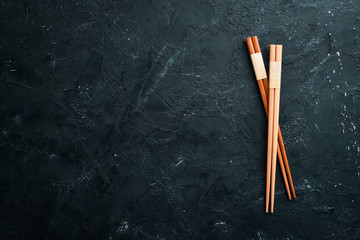 Wooden chopsticks on a black stone background. Top view. Free space for your text.