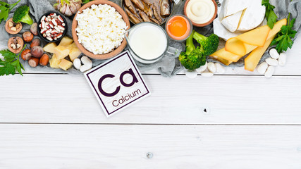 Food with calcium. A variety of foods rich in calcium: cheese, milk, parmesan, sour cream, fish, almonds, parsley, garlic, broccoli. On a white wooden background. Top view. Free copy space. - obrazy, fototapety, plakaty