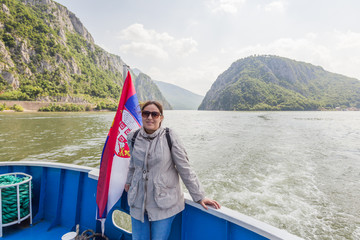 Portrait of smile tourist woman enjoy a cruise ship view of Danube river with Serbian national flag