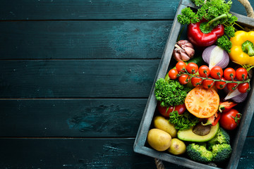 Fresh vegetables and fruits in a wooden box. Avocados, tomatoes, strawberries, melons, potatoes, paprika, citrus. Top view. Free space for your text.