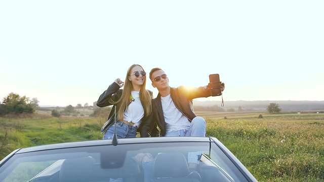 Attractive man and woman taking selfie while sitting in the cabriolet.