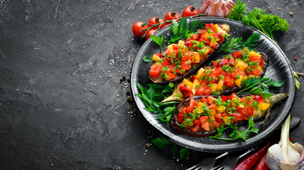 Eggplants baked with vegetables on a black plate. Top view. Free space for your text.