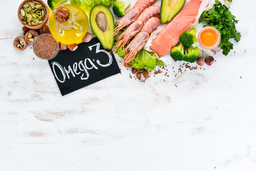 Foods containing omega 3. Vitamin Healthy foods: avocados, fish, shrimp, broccoli, flax, nuts, eggs, parsley. Top view. Free space for your text. On a white wooden background. - obrazy, fototapety, plakaty