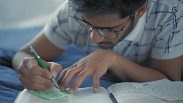 Close-Up, Indian Student in Glasses Makes Marks in the Cheat Sheet for the Upcoming Exam