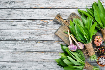 Fresh young wild garlic leaves on a white wooden background. Top view. Free space for your text.