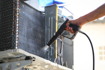 Technician cleaning air conditioner with water spray.
