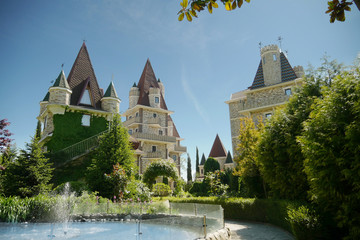 Fototapeta premium modern Victorian-style luxury hotel with a small fountain at the foot, beautiful well-kept trees against a blue sky in clear sunny weather