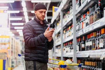 Young handsome man choosing wine in supermarket. Matter of wine choice.
