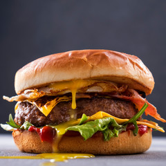 Tasty grilled beef burger with fried bacon and eggs, cheese, tomatoes and lettuce. Closeup. Macro...