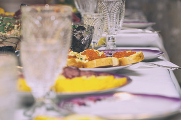 Festive table setting with crystal glasses and plates. Sandwiches with red caviar on the table. Selective focus