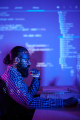 Serious bearded programmer sitting at the table and looking at computer monitor in dark room, he...