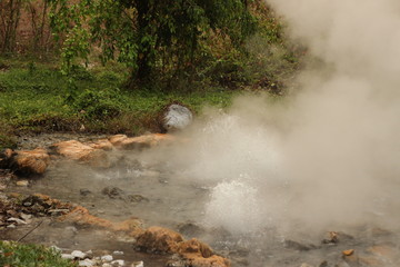 Naklejka na ściany i meble steam rising and rolling from the bubbling boiling water of a volcanic hot spring in a beautiful national park near Pai, Northern Thailand, Southeast Asia