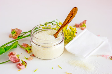 Cosmetic wax in a transparent jar near flower petals, plant leaves, face wipes, top view, flat lay