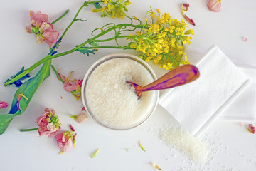 Cosmetic wax in a transparent jar near flower petals, plant leaves, face wipes, top view, flat lay