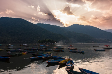 Pokhara lake at orange sunset with clouds and boats, Nepal