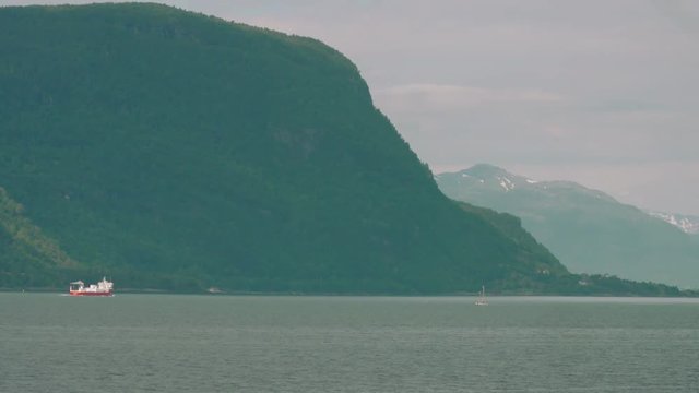 Large fishing vessel sailing in enourmous Fjord with high cliffs.