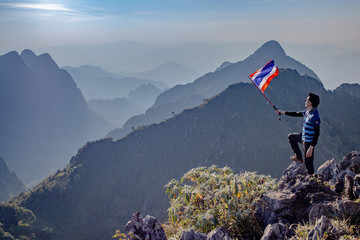 Asian trekking man holding Thailand flag  at the top of wildlife sanctuary name Doi Luang Chiang Dao with Shadow of mountain layer and sun ray.