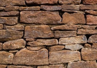 The wall is made of old, ancient stones, with plants growing from seams and cracks. close up.