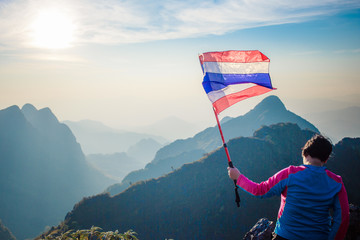 Woman Holding Thailand flag at the top of wildlife sanctuary name Doi Luang Chiang Dao, Thailand with Shadow of mountain layer and sun ray.