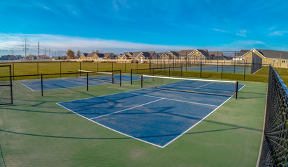 Tennis courts on a wide lush lawn underneath a vivid blue sky with clouds