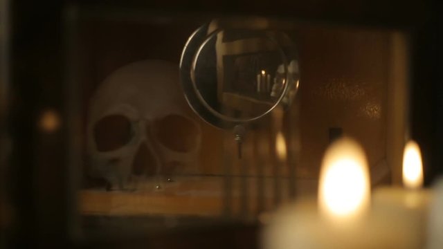 reflection of the skull and candles in the pendulum of an old clock
