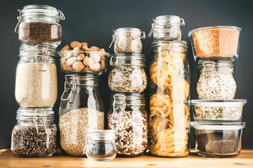 Assortment of grain products and pasta in glass storage containers on wooden table. Healthy...
