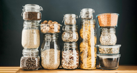 Assortment of uncooked grains, cereals and pasta in glass jars on wooden table. Healthy cooking,...