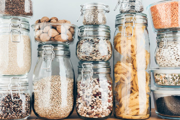 Assortment of uncooked grains, cereals and pasta in glass jars on wooden table. Healthy cooking,...