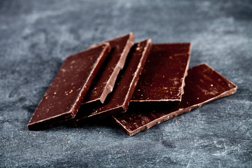 Chunks of broken dark chocolate stacked on grey background.