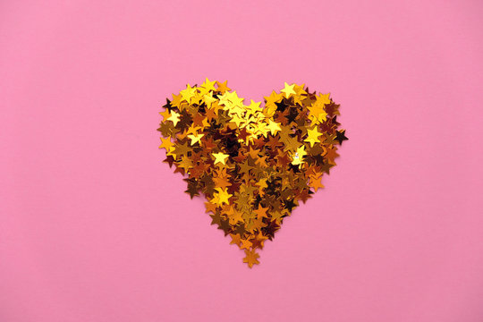 Gold sequins in the shape of a heart on a pink background