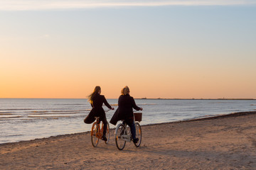   Women ride a bike along the seashore. Very beautiful sunset landscape. Great holiday by the sea. Evening bike ride.