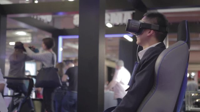 Man of Asian appearance, sitting on a chair with a headset and a virtual reality controller, uses virtual reality.